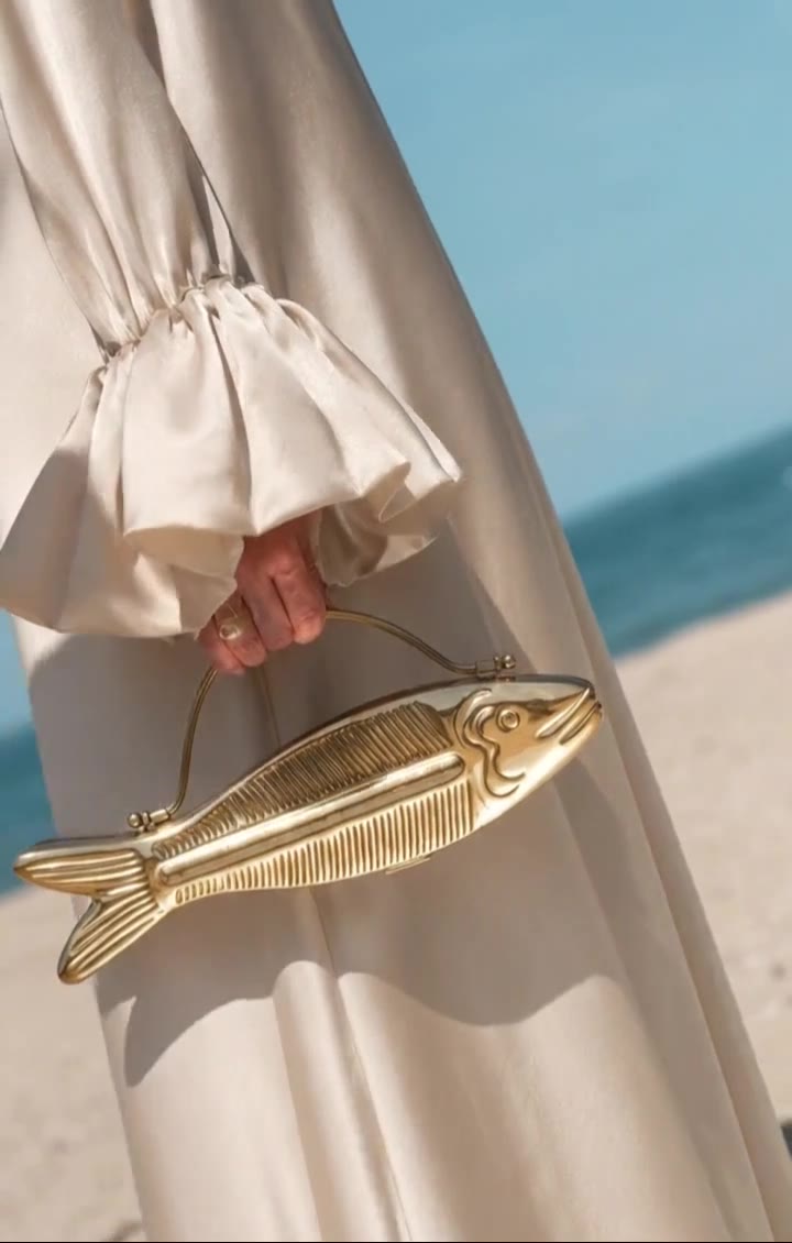 Azure Koi gold-finish fish-shaped clutch held by the beach, video preview